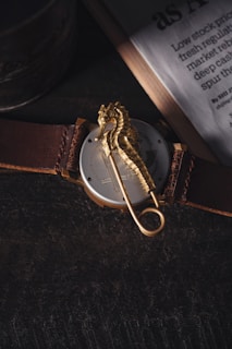 An elegant watch with a leather strap resting beside seashells on a sunlit beach.