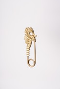 A gold-colored seahorse figurine integrated into the design of a safety pin, positioned against a plain white backdrop.