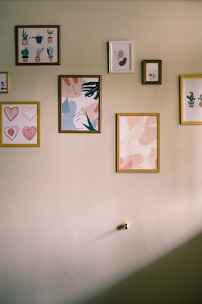 A wall adorned with several framed artworks, featuring abstract designs and illustrations of plants. The frames vary in size and color, and are neatly arranged, creating an aesthetically pleasing display.