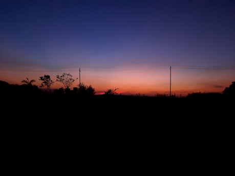 Залезно небе над селско българско поле с електропроводи, преминаващи през пейзажа.