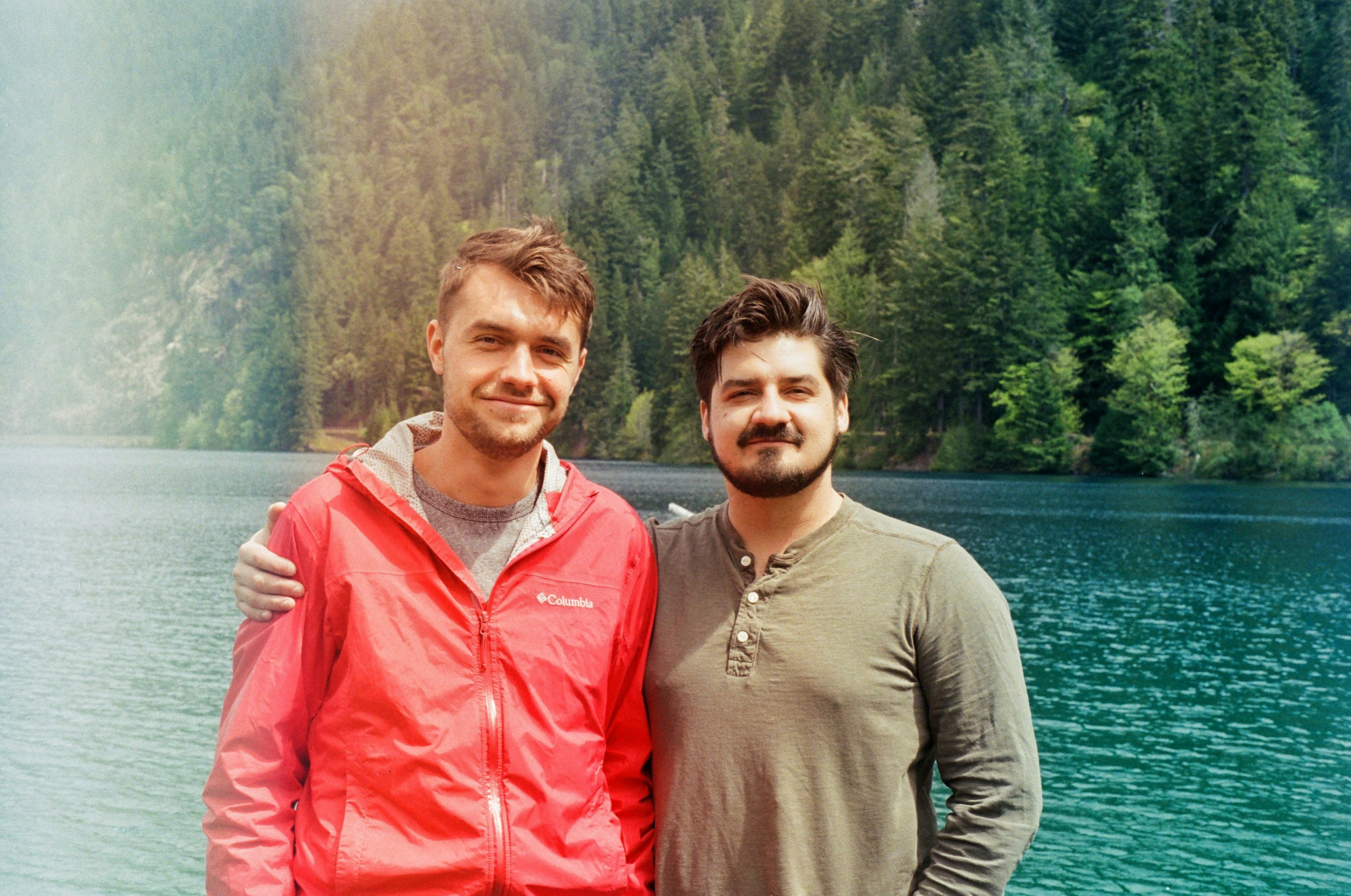 Two men standing next to each other in front of a lake photo – Free ...