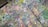 An abstract array of colorful paint splatters and drips covers a wooden surface, creating a chaotic and vibrant pattern. The paint layers overlap and blend, forming a rich tapestry of colors.