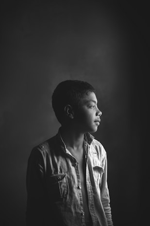 A moody black-and-white portrait of Saint Amari bathed in soft shadows, capturing a moment of quiet intensity.