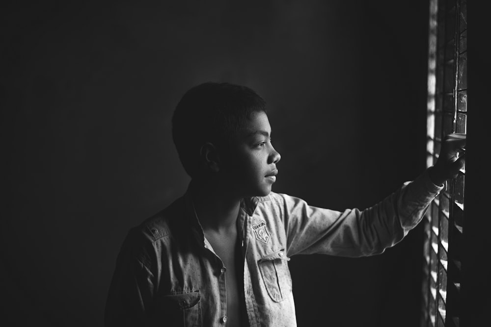 a black and white photo of a man looking out a window