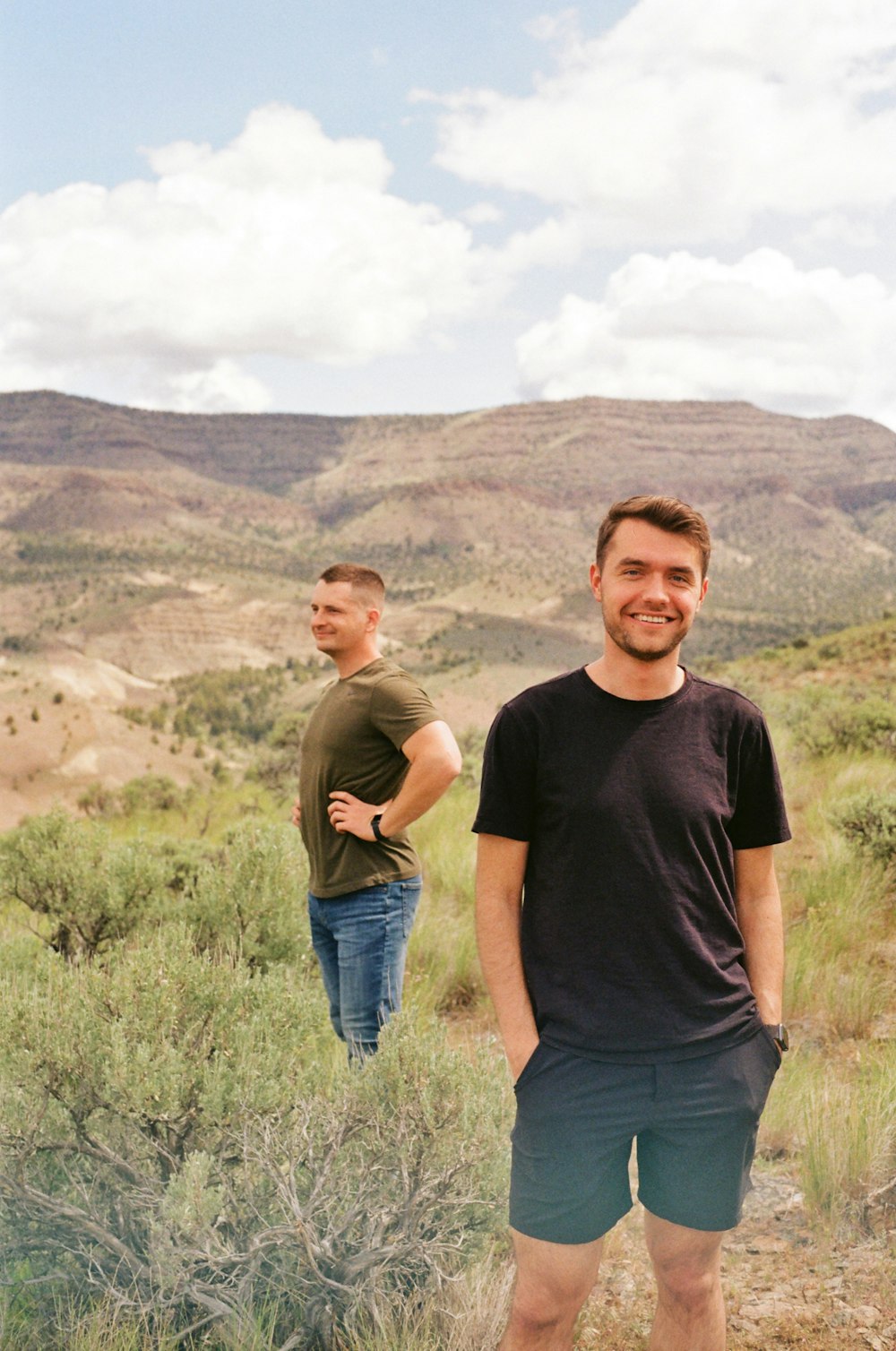 two men standing in a field with mountains in the background