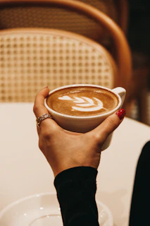 Close-up of hands with freshly manicured nails holding a cup of coffee in a cozy salon setting.