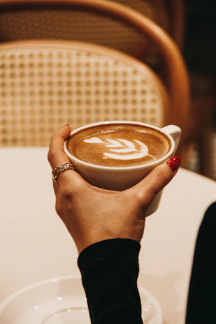 Close-up of hands with freshly manicured nails holding a cup of coffee in a cozy salon setting.