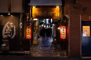A narrow alleyway lined with red lanterns glowing softly at dusk in a small Japanese town.