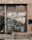 A storefront with a large window displays the words 'Smiths Home' and various white line drawings depicting household items and plants. Outside, there is a wooden bench and several potted plants. The building has a tiled facade with various stickers on the door frame.