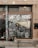 A storefront with a large window displays the words 'Smiths Home' and various white line drawings depicting household items and plants. Outside, there is a wooden bench and several potted plants. The building has a tiled facade with various stickers on the door frame.