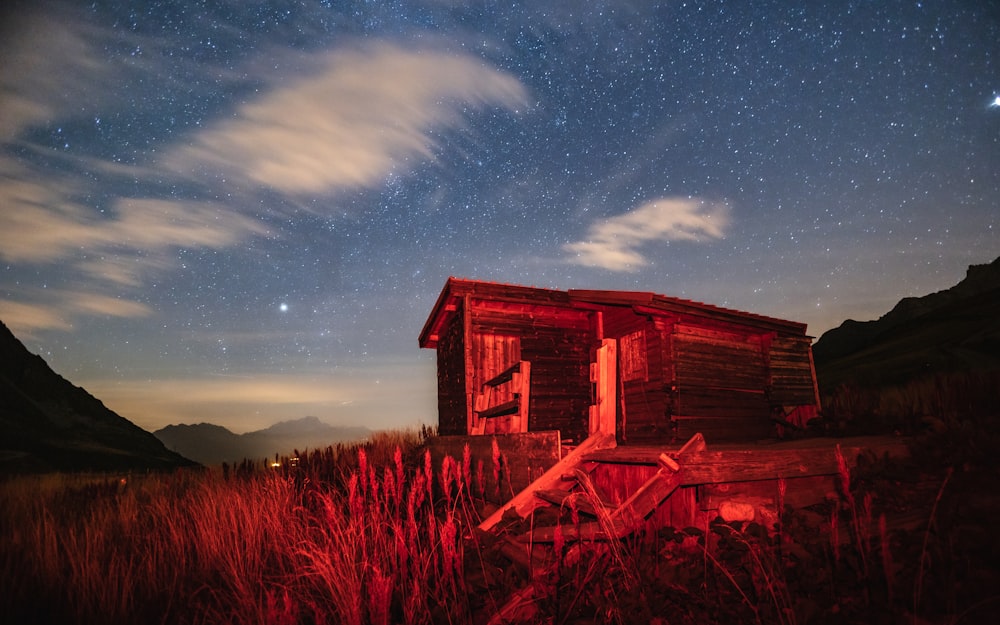 a cabin in the middle of a field under a night sky filled with stars