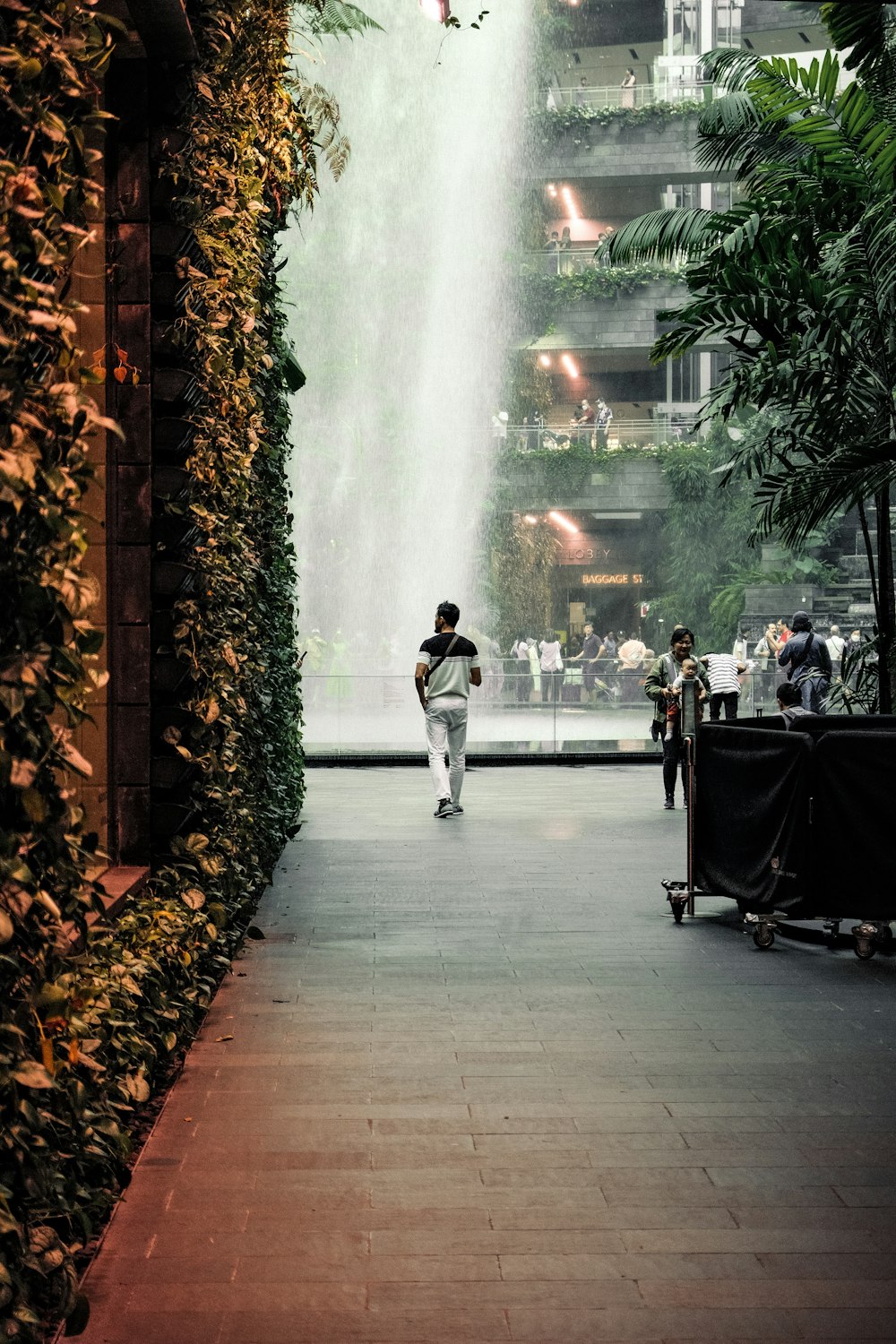 a man walking down a sidewalk next to a tall waterfall