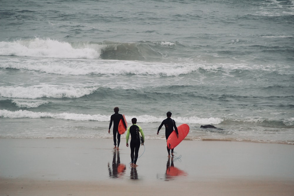three surfers walking on the beach with their surfboards