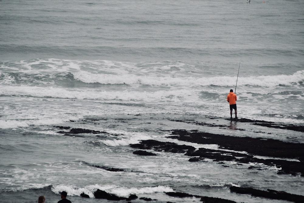 a man standing on top of a rocky beach next to the ocean