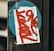 A close-up of a postal label with red graffiti text placed on a black surface with a blue circular background. The label has visible printed text and barcode.