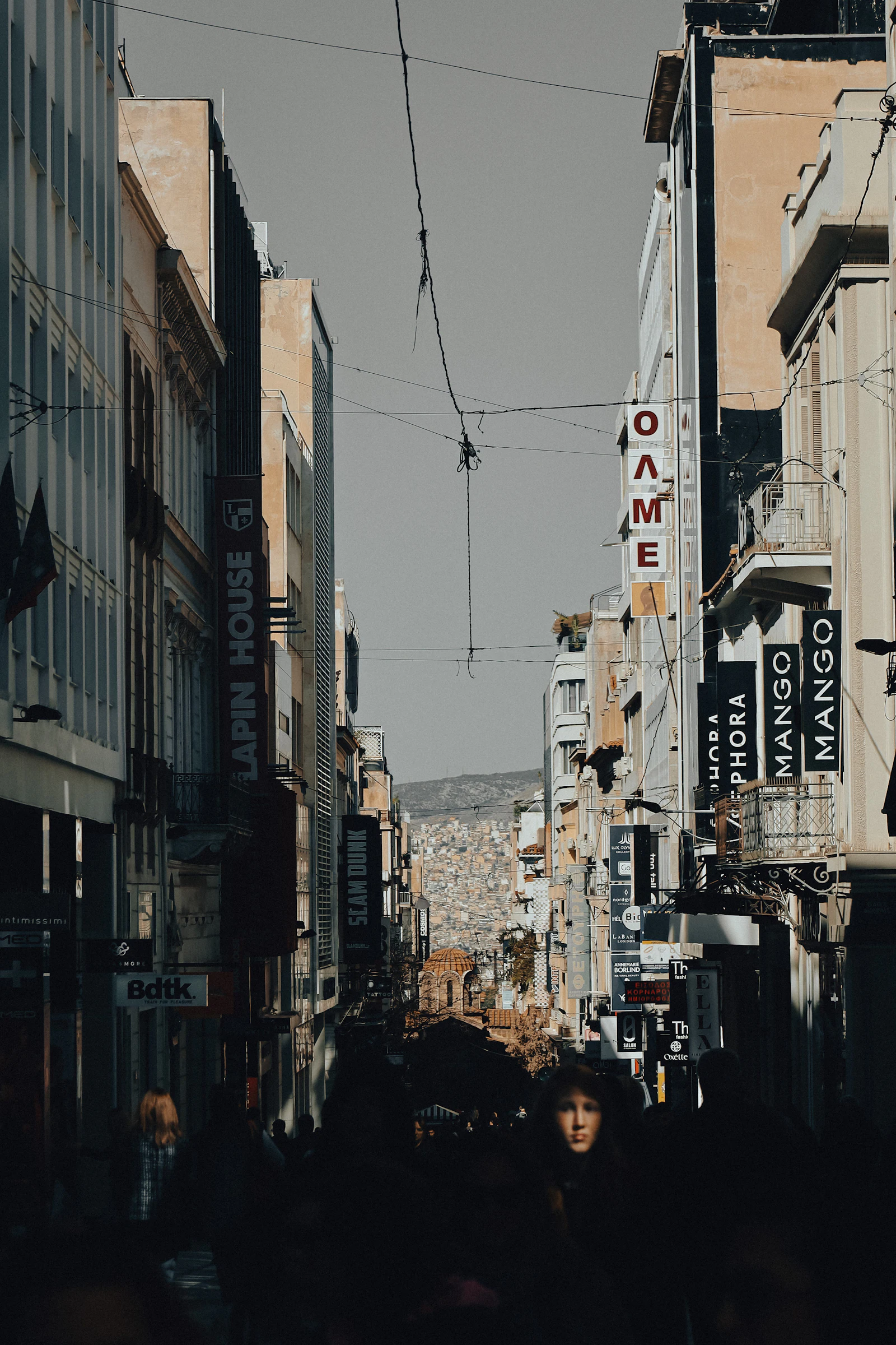 People walking a downtown sidewalk past low buildings.