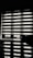 Horizontal blinds partially cover a window, creating a pattern of alternating light and shadow. Below the window, there is a reflective surface, possibly a table, displaying the same pattern along with a few small objects.