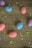 Colorful speckled eggs in pink, blue, and purple are scattered on a wooden surface, surrounded by green and red sprinkles and white star-shaped decorations.