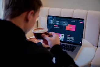 a man sitting in front of a laptop computer holding a cup of coffee