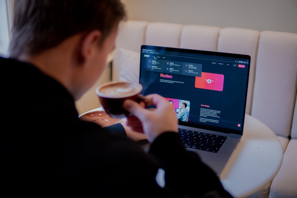 a man sitting in front of a laptop computer holding a cup of coffee