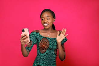a woman holding a cell phone in front of a pink background