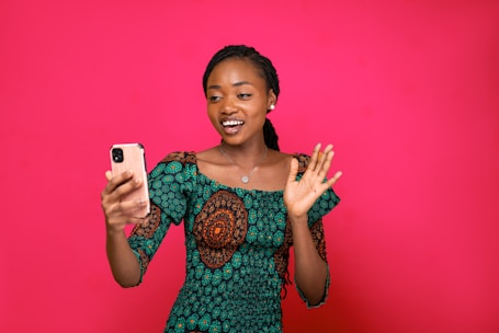 a woman holding a cell phone in front of a pink background