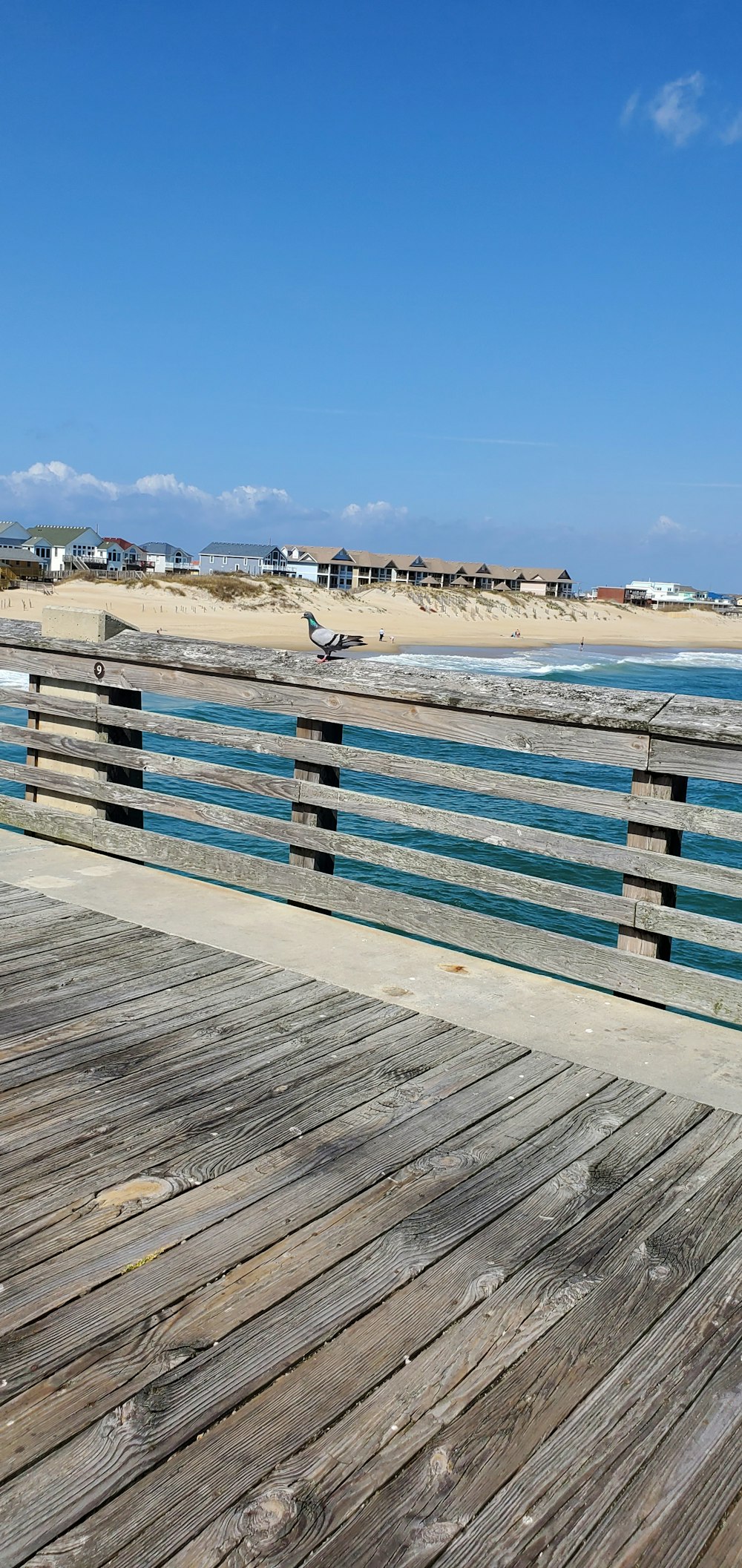 a wooden boardwalk next to a beach with houses in the background