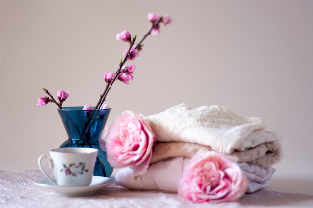 a blue vase with pink flowers next to a cup and saucer