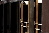 A close-up view of several gold-colored metal doors with vertical handles, set within a dark frame. The doors have reflective glass panels that are partially shaded, suggesting a quiet or closed-off environment. The lighting emphasizes the metallic sheen of the door handles and frames.