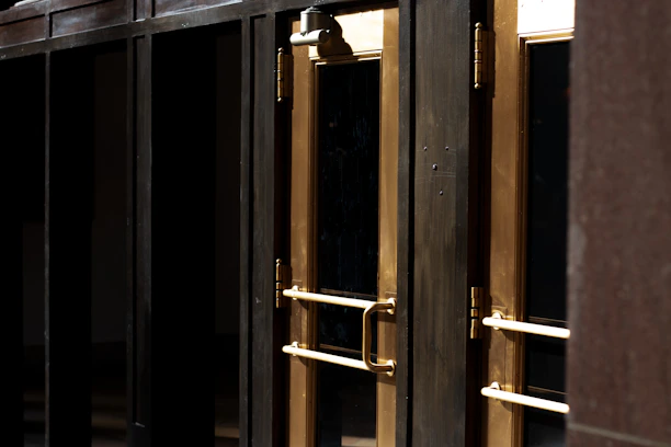 Close-up of a matte black steel security door with brushed steel accents and a gold handle, set against a dark luxury background.