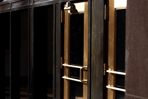 A close-up view of several gold-colored metal doors with vertical handles, set within a dark frame. The doors have reflective glass panels that are partially shaded, suggesting a quiet or closed-off environment. The lighting emphasizes the metallic sheen of the door handles and frames.