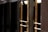 A close-up view of several gold-colored metal doors with vertical handles, set within a dark frame. The doors have reflective glass panels that are partially shaded, suggesting a quiet or closed-off environment. The lighting emphasizes the metallic sheen of the door handles and frames.