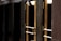A close-up view of several gold-colored metal doors with vertical handles, set within a dark frame. The doors have reflective glass panels that are partially shaded, suggesting a quiet or closed-off environment. The lighting emphasizes the metallic sheen of the door handles and frames.