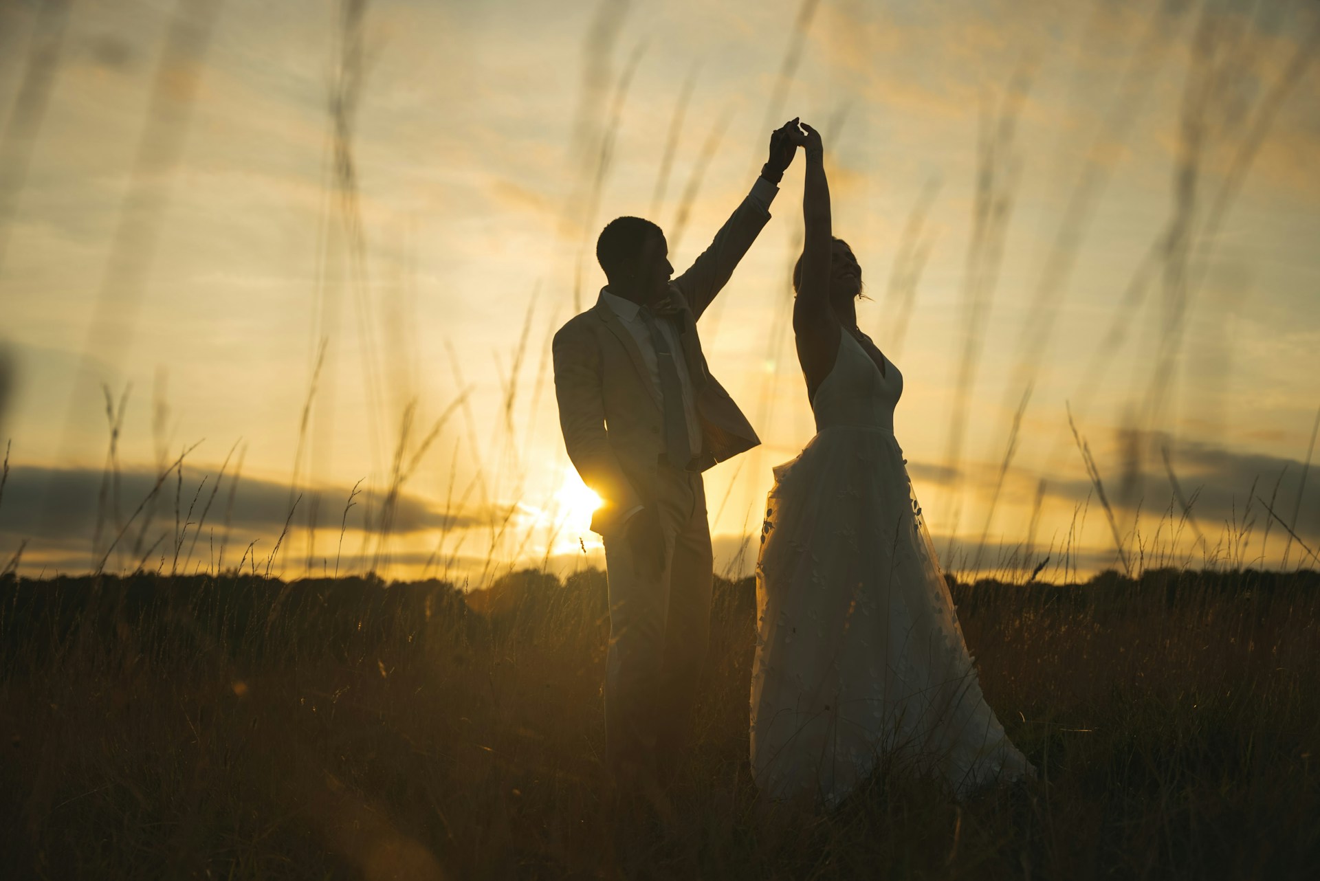 a bride and groom dancing in a field at sunset