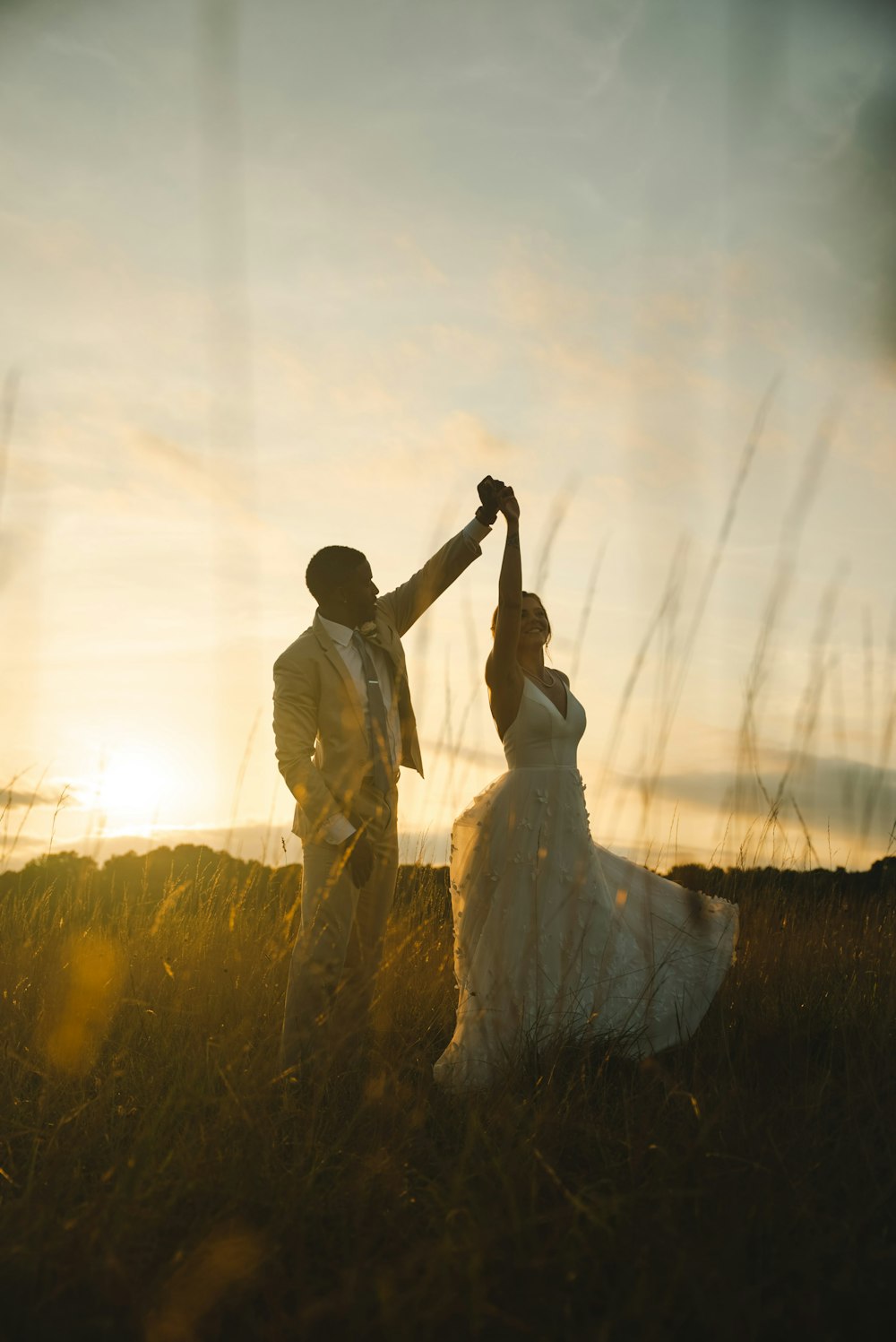 a bride and groom dancing in a field at sunset
