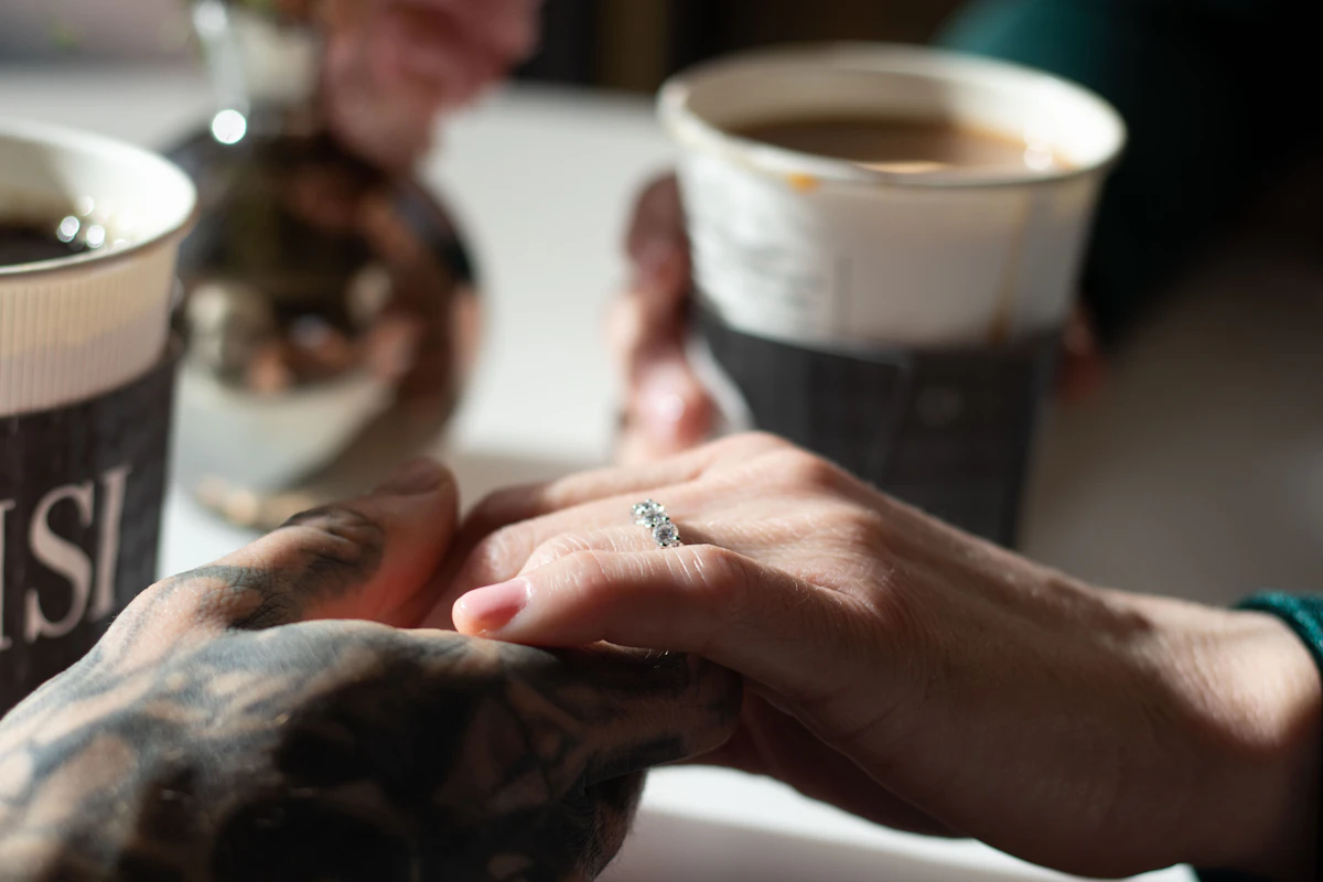 Dos personas se toman de las manos junto a una taza de café.