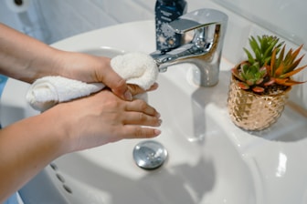 Close-up of hands scrubbing a spotless bathroom sink with eco-friendly products