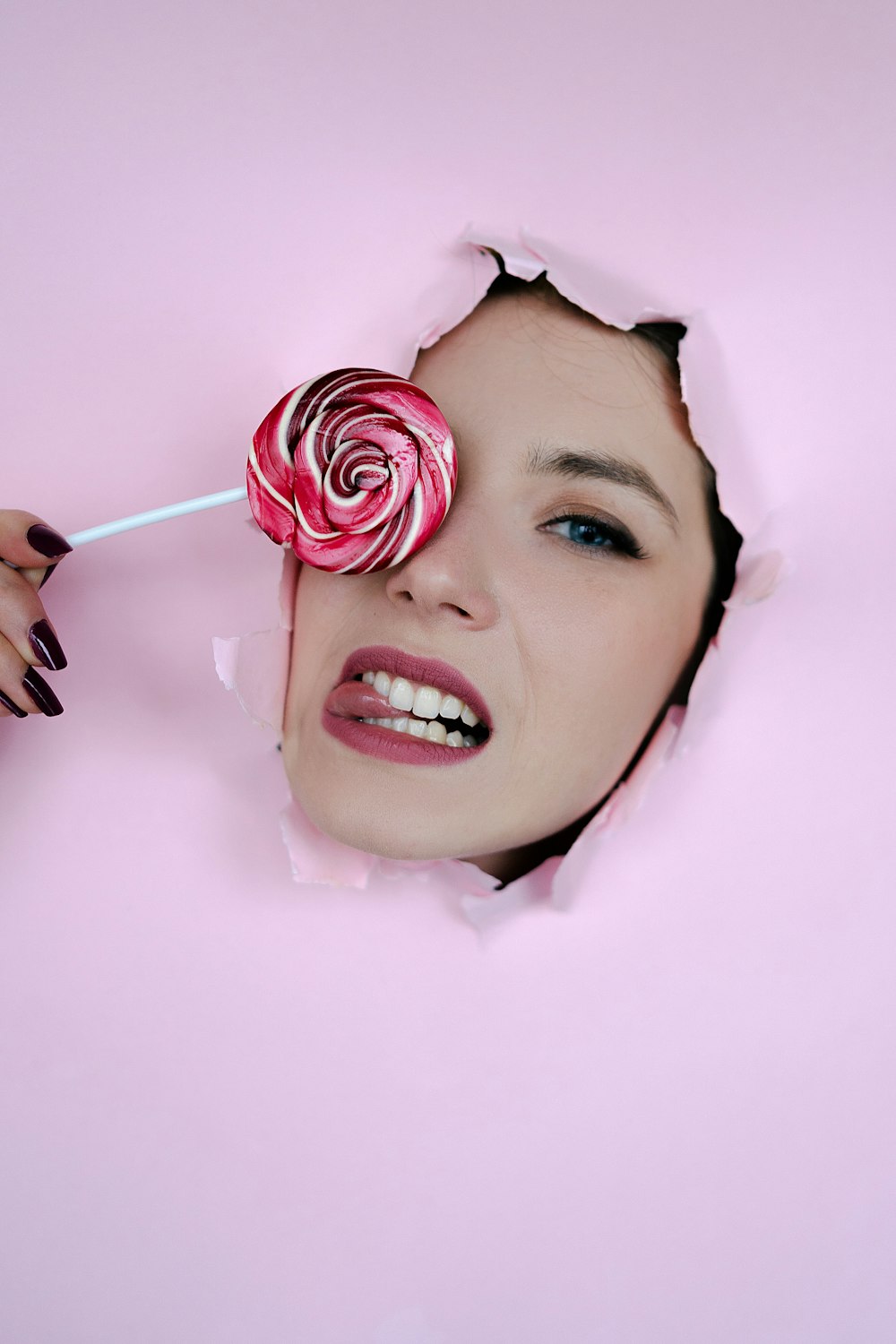 a woman holding a lollipop in her mouth through a hole