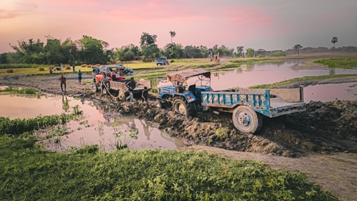 Tow truck assisting a car stuck in mud on a rural road.