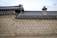 A traditional Korean wall features intricate geometric patterns with a hexagonal design in shades of beige and grey. The roof is topped with dark grey curved tiles, and there is a small decorative chimney visible.