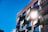 A modern apartment building with a brick facade, featuring large windows and multiple balconies. The sun is shining brightly, reflecting off the windows and casting a stark light on the structure. The sky is clear and vividly blue.