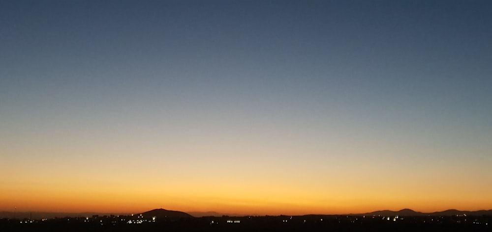 the sun is setting over a city with mountains in the background