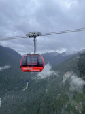 a red cable car in the middle of a mountain