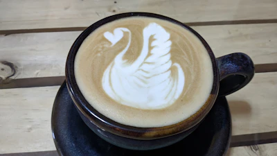 Latte art dengan pola swan yang detail di atas cangkir kopi putih.