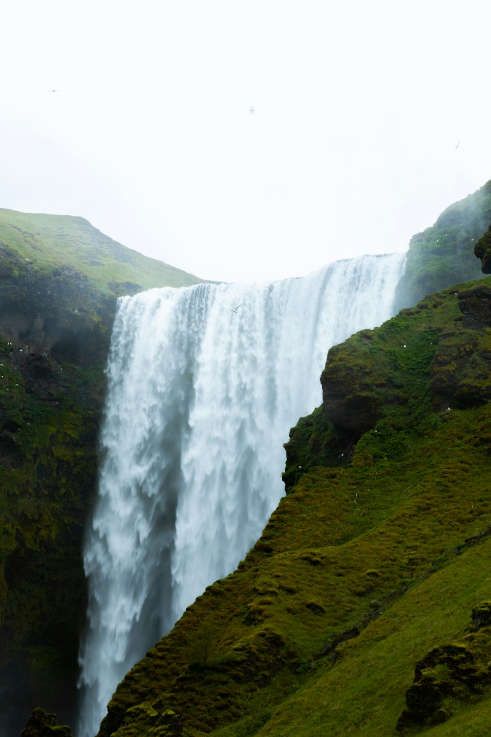 a very tall waterfall in the middle of a lush green field