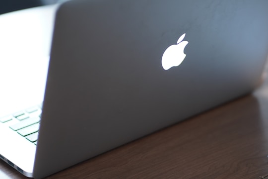 A laptop with a glowing logo on the back of the screen, placed on a wooden surface. The focus is on the illuminated logo, and the keyboard is partially visible.