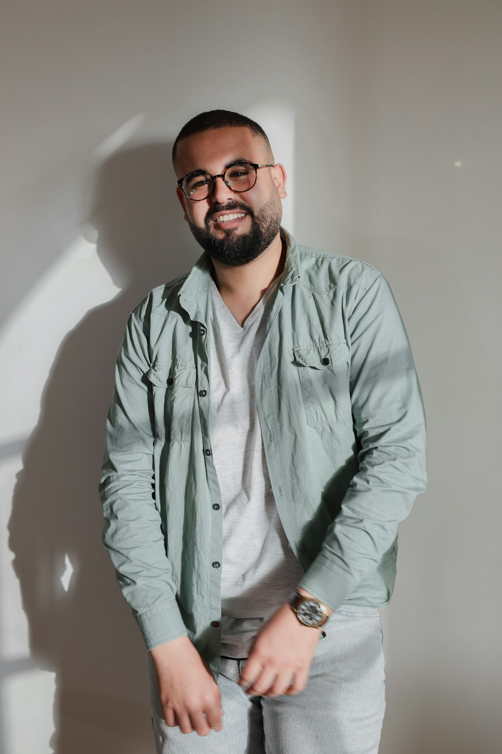 a man with a beard and glasses standing in front of a wall