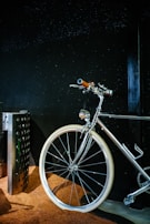A sleek, shiny bicycle with a chrome finish is positioned against a dark background. The handlebars and a part of the frame are highlighted, with white tires standing out against a textured brown surface beneath.