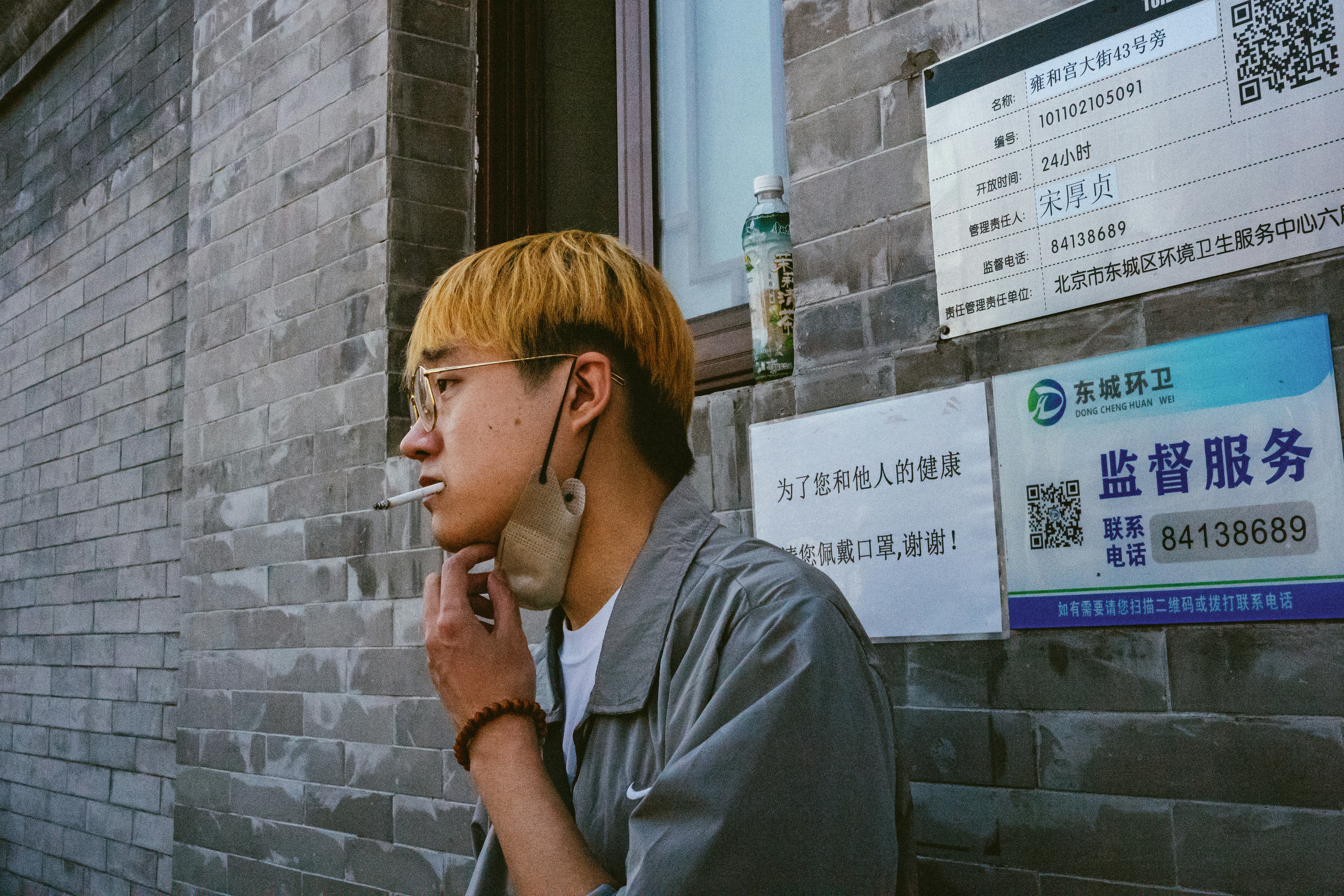 a man smoking a cigarette in front of a brick building
