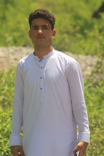A casual outdoor shot of a man in off-white traditional wear, embodying simplicity.